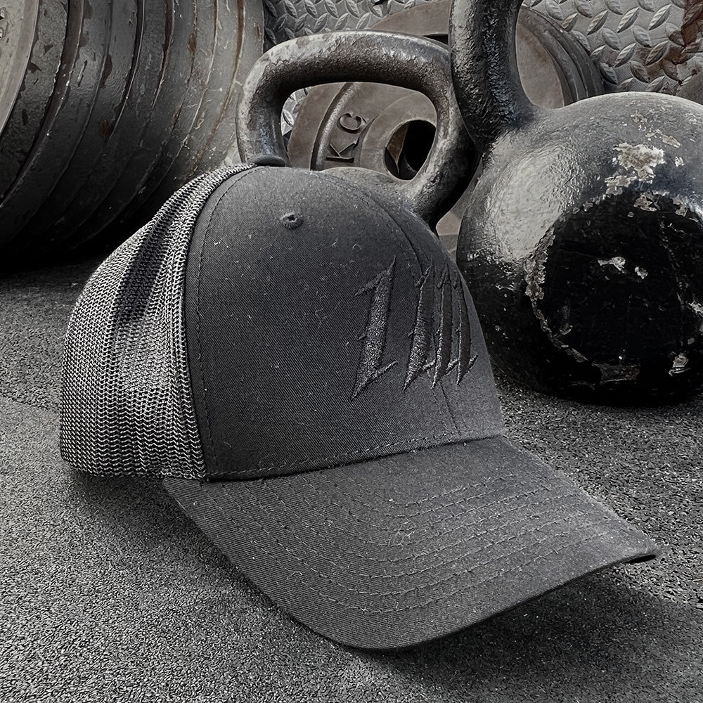 Blacked Out Trucker Cap, on a gym floor beside kettlebells